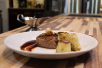 Filet Mignon with Demi-Glace Sauce Seared filet mignon with demi-glace sauce, roasted garlic, rosemary, and potato wedges on a white plate.