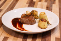 Seared Filet Mignon with Demi-Glace Sauce, fondant potatoes, and rosemary on a white plate