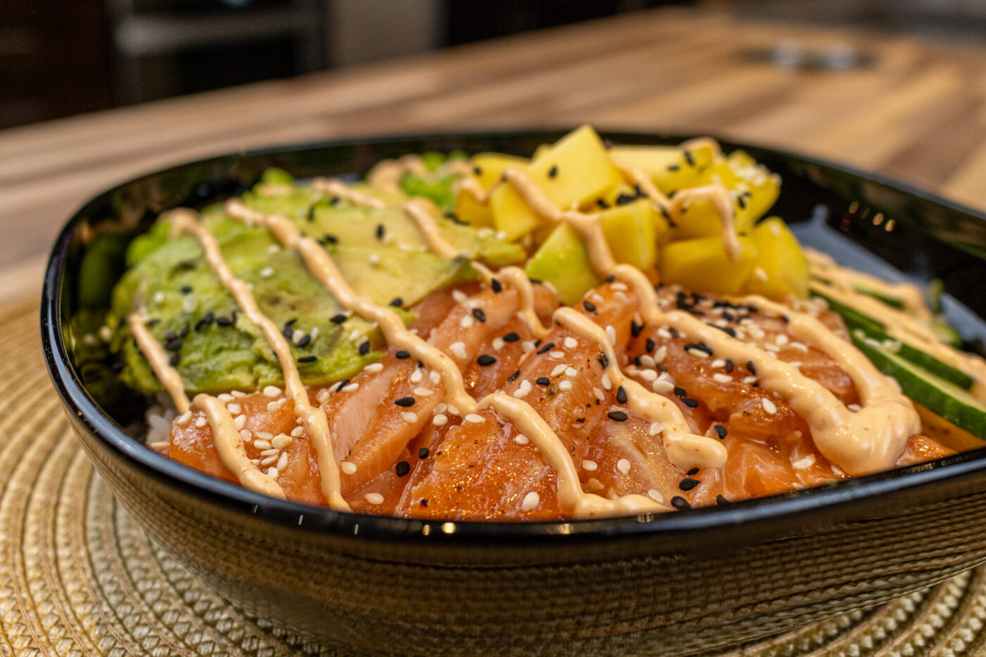 Poke Bowl with Salmon Black bowl of Poke Bowl with Salmon topped with avocado, mango, sesame seeds and creamy drizzle.