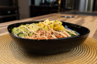 Poke Bowl with Salmon Black bowl of Poke Bowl with Salmon topped with mango, avocado, and spicy mayo drizzle.