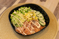 Poke Bowl with Salmon Poke Bowl with Salmon in a black dish with salmon, avocado, mango, cucumber, and spicy mayo.