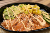 Poke Bowl with Salmon Poke Bowl with Salmon in a black bowl with salmon, avocado, mango, cucumber, sesame seeds, and spicy mayo.