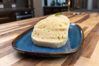 Czech Bread Dumpling Houskovy Knedlik Recipe Sliced houskový knedlík with bubbly interior and herb garnish on a blue plate.