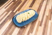 Czech Bread Dumpling Houskovy Knedlik Recipe Sliced rounds of houskový knedlík arranged on a blue oval plate, garnished with a small herb sprig.
