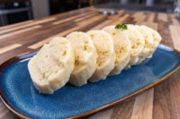 Czech Bread Dumpling Houskovy Knedlik Recipe Sliced houskový knedlík rounds on a blue plate, garnished with a parsley leaf.
