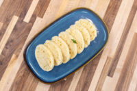 Czech Bread Dumpling Houskovy Knedlik Recipe Sliced rounds of houskový knedlík with a spongy, holey texture, fanned on a dark blue oval plate.