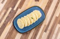 Czech Bread Dumpling Houskovy Knedlik Recipe Sliced houskový knedlík rounds fanned on a blue oval plate with a parsley garnish on a wood table.