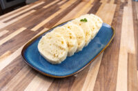 Czech Bread Dumpling Houskovy Knedlik Recipe Sliced houskový knedlík rounds with visible air pockets, fanned on a blue oval plate on a wooden table.