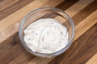 Garlic Dipping Sauce for Pretzels Glass bowl of Garlic Dipping Sauce for Pretzels, creamy with dark herb flecks, on a wood surface.