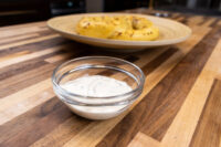 Garlic Dipping Sauce for Pretzels Glass bowl of Garlic Dipping Sauce for Pretzels with herb flecks, pretzels on a plate behind it