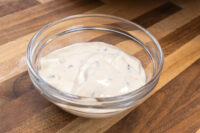 Garlic Dipping Sauce for Pretzels Glass bowl of creamy Garlic Dipping Sauce for Pretzels with visible chive flecks on a wooden surface.