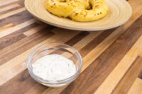 Garlic Dipping Sauce for Pretzels Glass bowl of Garlic Dipping Sauce for Pretzels with visible chive flecks, pretzel rolls on a wooden plate behind it