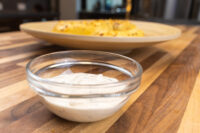 Garlic Dipping Sauce for Pretzels Glass bowl of Garlic Dipping Sauce for Pretzels, creamy with dark chive flecks, on a wood table.