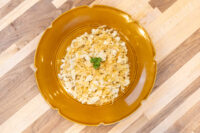 Halušky with Sauerkraut Plated Halušky with Sauerkraut, pale shredded dumplings topped with parsley on a mustard ceramic plate.