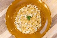Halušky with Sauerkraut Overhead view of Halušky with Sauerkraut in a mustard-yellow ceramic bowl, showing soft potato dumplings mixed with shredded sauerkraut and a parsley garnish, set on a wooden surface.