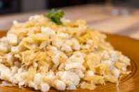 Halušky with Sauerkraut A gold-rimmed plate piled with soft Halušky with Sauerkraut, the pale dumplings mixed with golden strands and topped with a sprig of parsley.