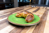 A single golden Loupáčky Czech Poppy Seed Crescent topped with poppy seeds on a green plate.