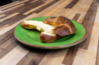 A poppy seed-topped Loupáčky Czech Poppy Seed Crescent, sliced open, on a green plate atop a wooden table.