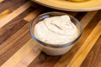 Glass bowl of Mustard Dipping Sauce for Soft Pretzels, creamy and speckled, on a wooden counter.