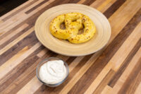 Bowl of Mustard Dipping Sauce for Soft Pretzels beside a seeded soft pretzel on a wooden plate.