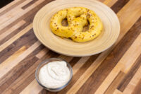 Glass bowl of speckled creamy Mustard Dipping Sauce for Soft Pretzels beside two golden pretzels on a wooden plate