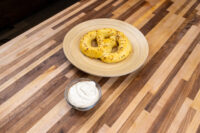 Bowl of Mustard Dipping Sauce for Soft Pretzels beside a seasoned pretzel on a round wooden plate