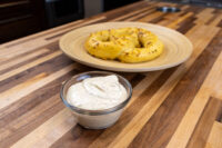 Small glass bowl of Mustard Dipping Sauce for Soft Pretzels beside a plate of pretzels.