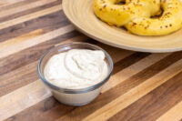 Small glass bowl of Mustard Dipping Sauce for Soft Pretzels beside a plate of seasoned pretzels on a wooden table