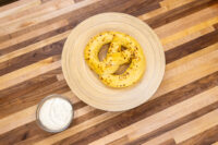 Small bowl of Mustard Dipping Sauce for Soft Pretzels beside a golden pretzel on a wooden plate.