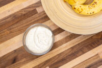 Glass bowl of Mustard Dipping Sauce for Soft Pretzels beside golden bread rings on a wooden board.