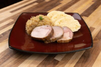Pork-Sauerkraut-Dumpling (Vepřo-knedlo-zelo): pork slices, sauerkraut, and dumpling slices on a red plate.