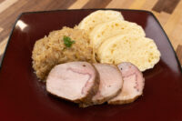 Sliced pork, sauerkraut, and dumpling slices arranged on a dark red plate for Pork-Sauerkraut-Dumpling