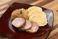 Sliced pork, sauerkraut, and dumpling rounds arranged on a dark red plate for Pork-Sauerkraut-Dumpling (Vepřo-knedlo-zelo)