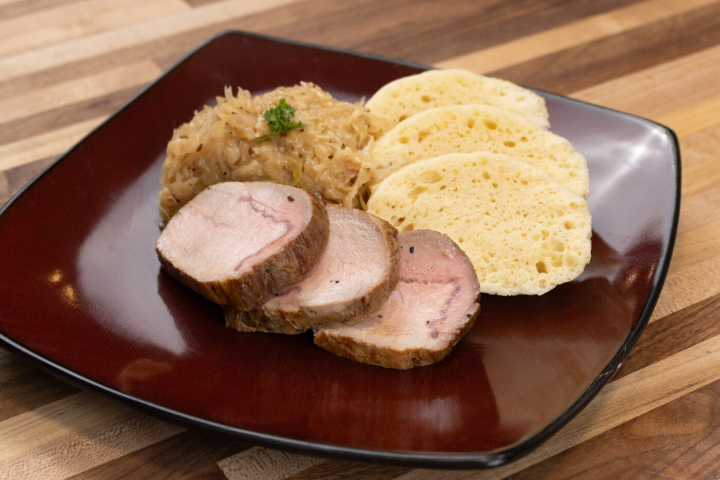 Sliced pork, sauerkraut, and dumpling slices for Pork-Sauerkraut-Dumpling (Vepřo-knedlo-zelo) on a red plate