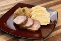 Pork-Sauerkraut-Dumpling Plate Sliced pork, sauerkraut, and dumpling slices for Pork-Sauerkraut-Dumpling (Vepřo-knedlo-zelo) on a red plate