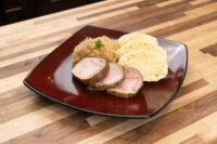 Sliced pork, sauerkraut, and dumpling rounds of Vepřo-knedlo-zelo on a dark square plate.