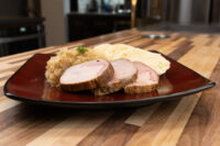 Plate of Pork-Sauerkraut-Dumpling (Vepřo-knedlo-zelo) with sliced pork, cabbage, and dumpling on a dark plate.