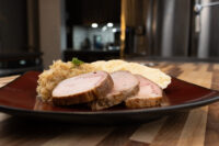 Sliced pork, sauerkraut, and knedlík dumpling arranged on a dark red plate for Vepřo-knedlo-zelo