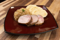 Sliced Pork-Sauerkraut-Dumpling (Vepřo-knedlo-zelo) with sauerkraut and dumpling slices on a dark red plate.