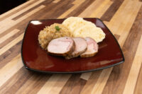 Sliced pork, sauerkraut, and dumpling scoops plated together for Vepřo-knedlo-zelo on a dark red plate.