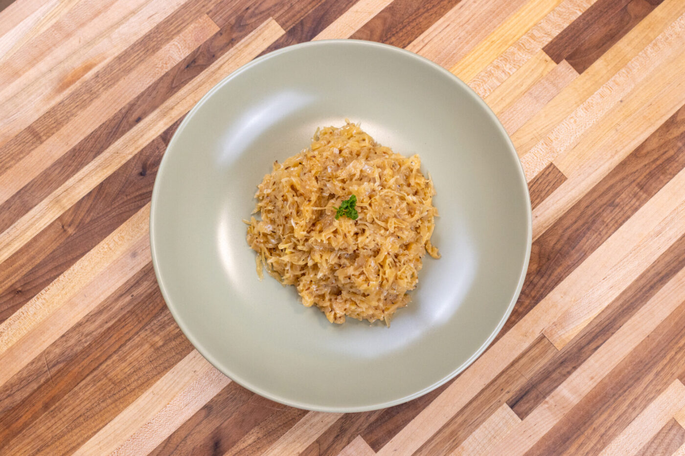 Sauerkraut (Kysane Zelí) Bowl of golden sautéed Sauerkraut (Kysane Zelí) topped with a small herb garnish on a striped wooden table.