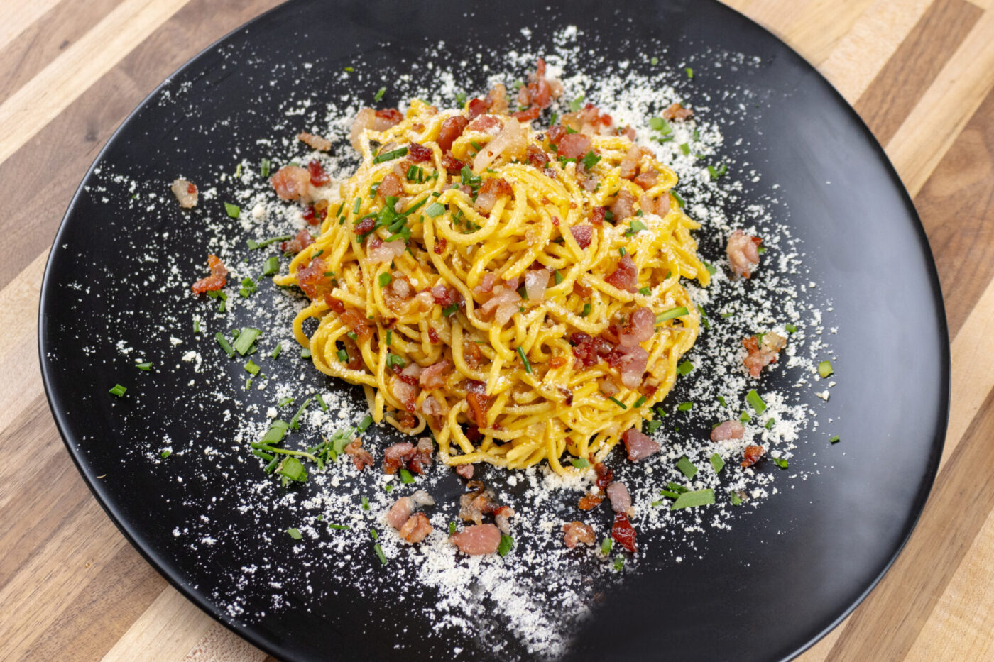 Spaghetti Carbonara Spaghetti Carbonara with golden egg sauce, crispy bacon bits, herbs, and grated cheese on a black plate