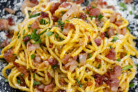 Spaghetti Carbonara Spaghetti Carbonara tossed with crispy bacon, herbs, and cheese on a dark speckled plate.