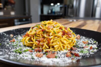 Spaghetti Carbonara Golden spaghetti carbonara with crispy bacon bits, grated cheese, and herbs on a black plate
