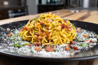 Spaghetti Carbonara Plated Spaghetti Carbonara with crispy bacon bits, herbs, and grated cheese on a black plate