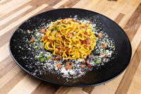 Spaghetti Carbonara Plate of Spaghetti Carbonara with bacon bits, herbs, and grated cheese on a black dish.