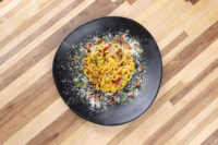 Spaghetti Carbonara Spaghetti Carbonara twirled on a black plate, topped with bacon bits, herbs, and grated cheese.