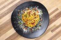 Spaghetti Carbonara Spaghetti Carbonara twirled on a black plate with creamy orange sauce, bacon bits, herbs, and grated cheese