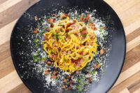 Spaghetti Carbonara Overhead view of Spaghetti Carbonara with crisp bacon bits, herbs, and grated cheese on a black plate.