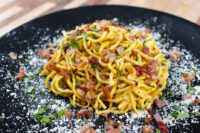 Spaghetti Carbonara Twirled Spaghetti Carbonara with bacon bits, herbs, and grated cheese on a black plate.
